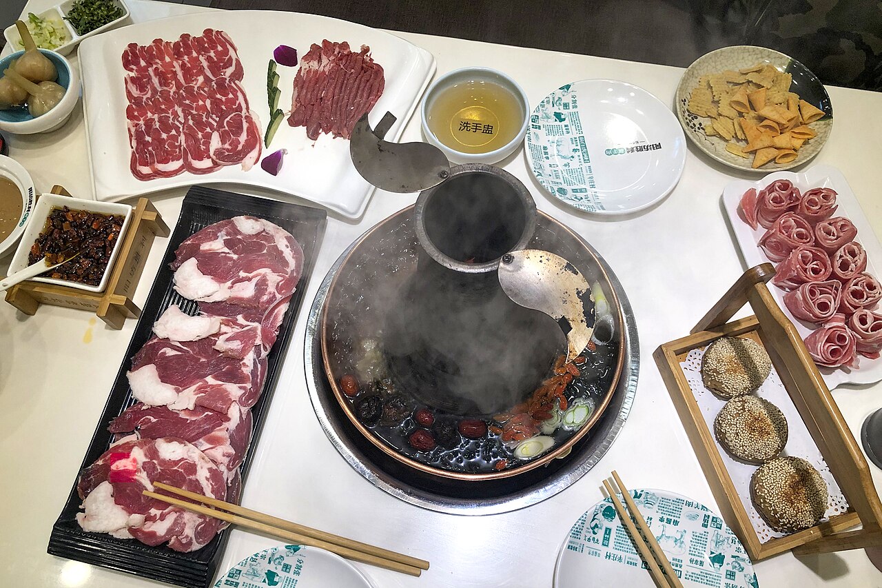 Overhead spread of copper-pot mutton hotpot, raw lamb and accompaniments
