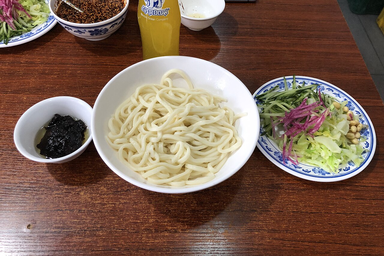 Bowl of noodles, dark sauce and assorted vegetable toppings for zhajiangmian