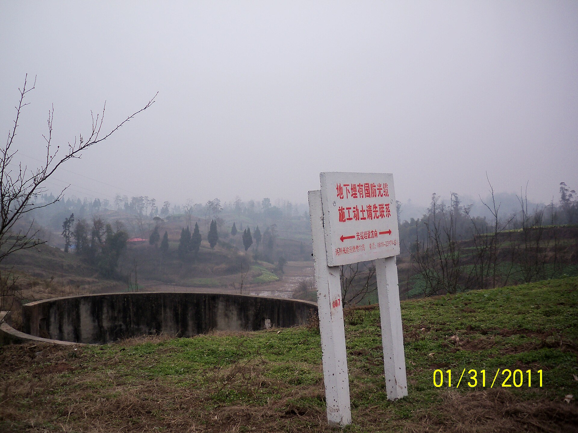 Bare orchard trees, fields, and infrastructure sign in rural Dazhu