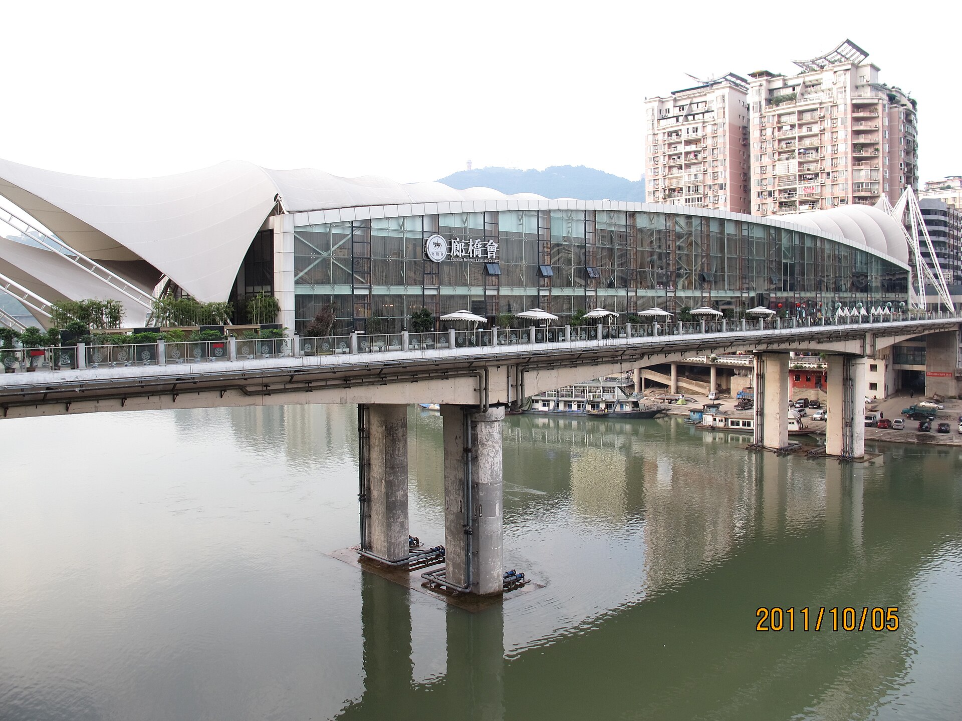 Glazed mixed-use enclosure carried above the river on a Dazhou bridge