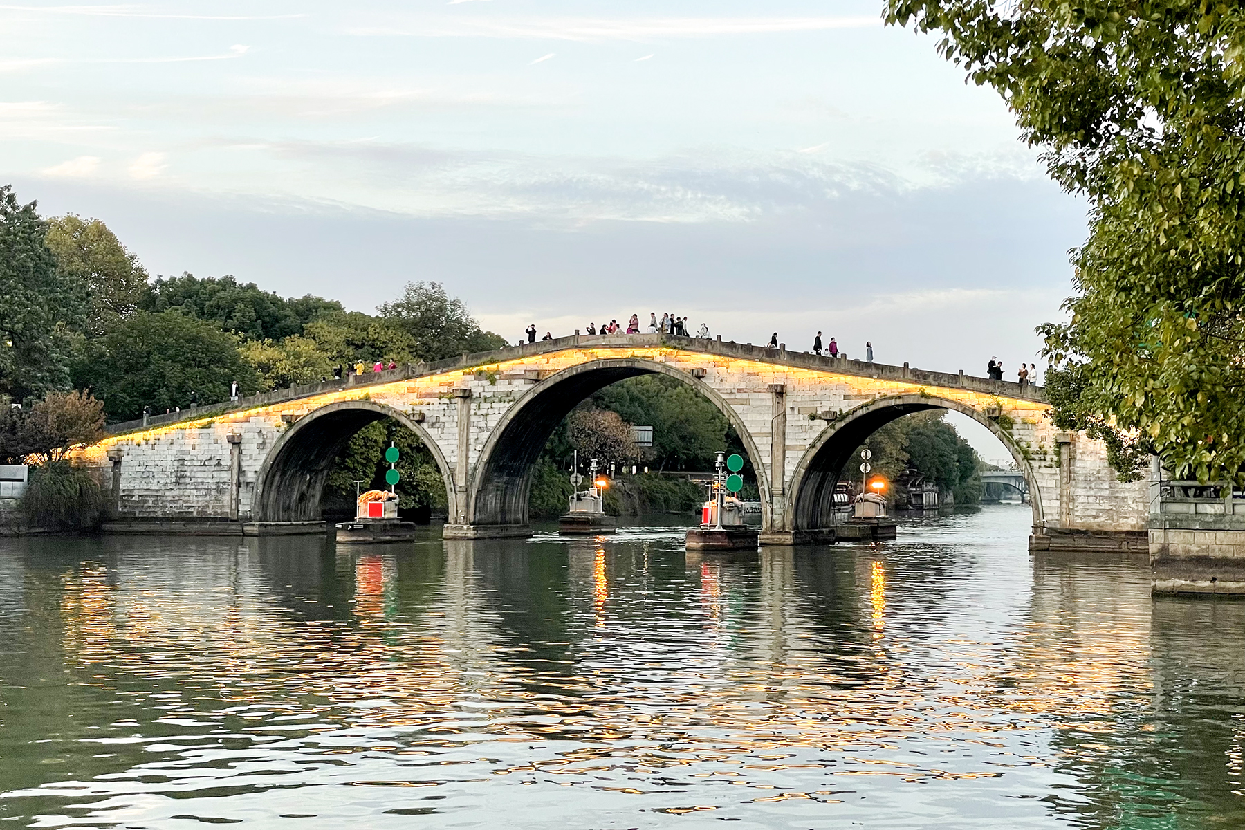Three-arch Gongchen Bridge with pedestrians and working boats at dusk