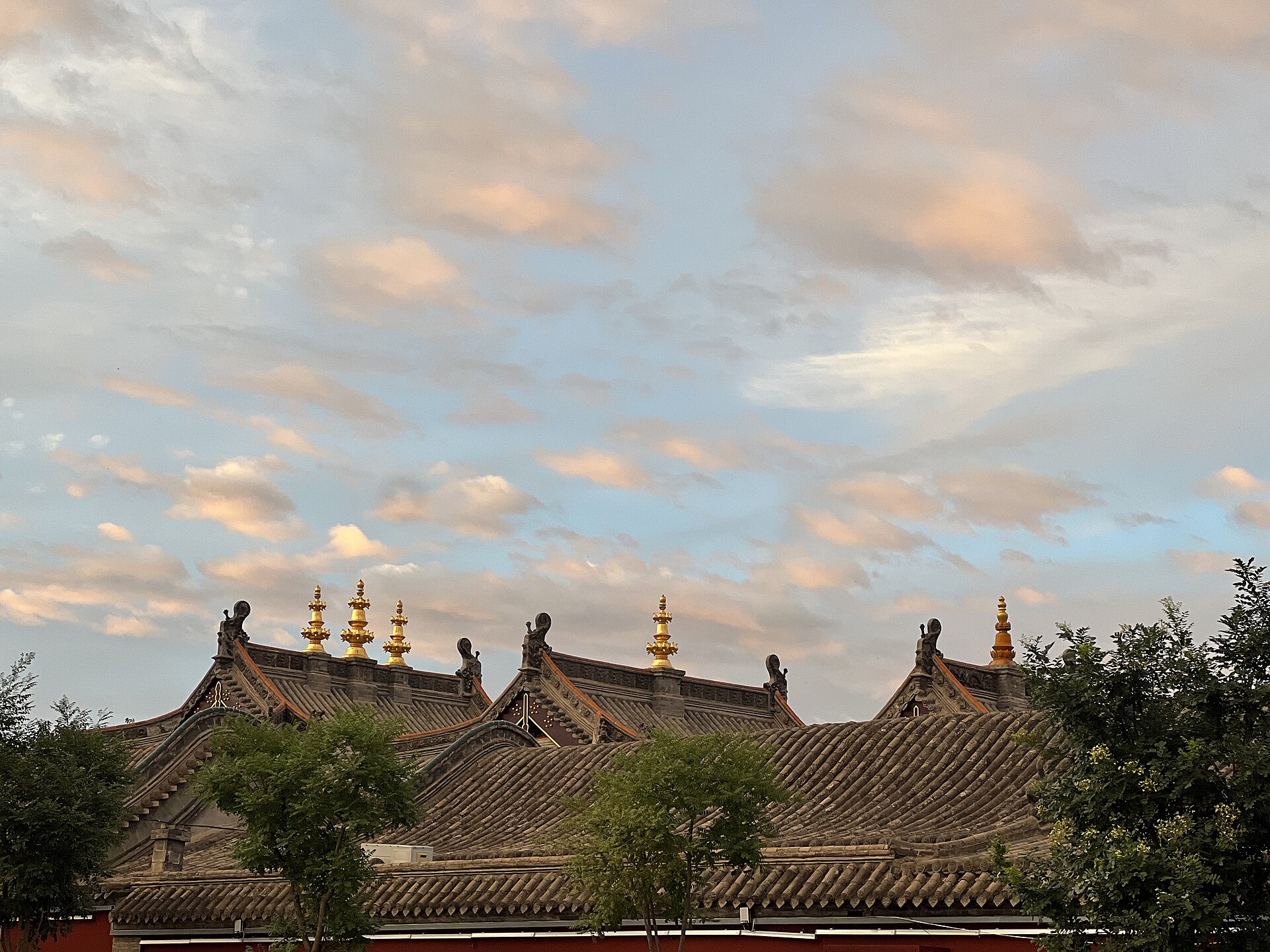 Grey tiled roofs and gilded finials at Dazhao beneath warm evening cloud