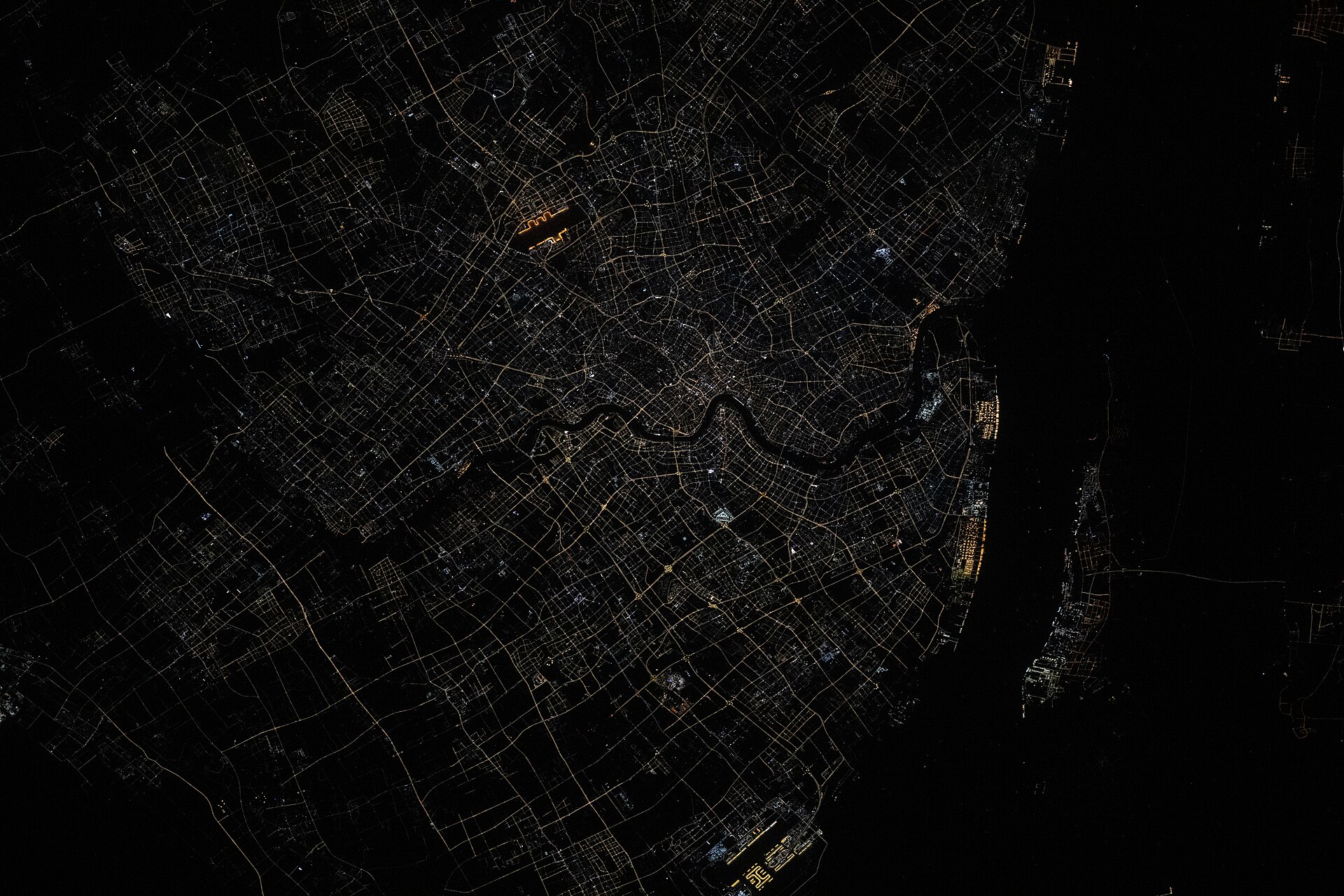 Orbital night view of Shanghai's illuminated street grid and dark Huangpu River