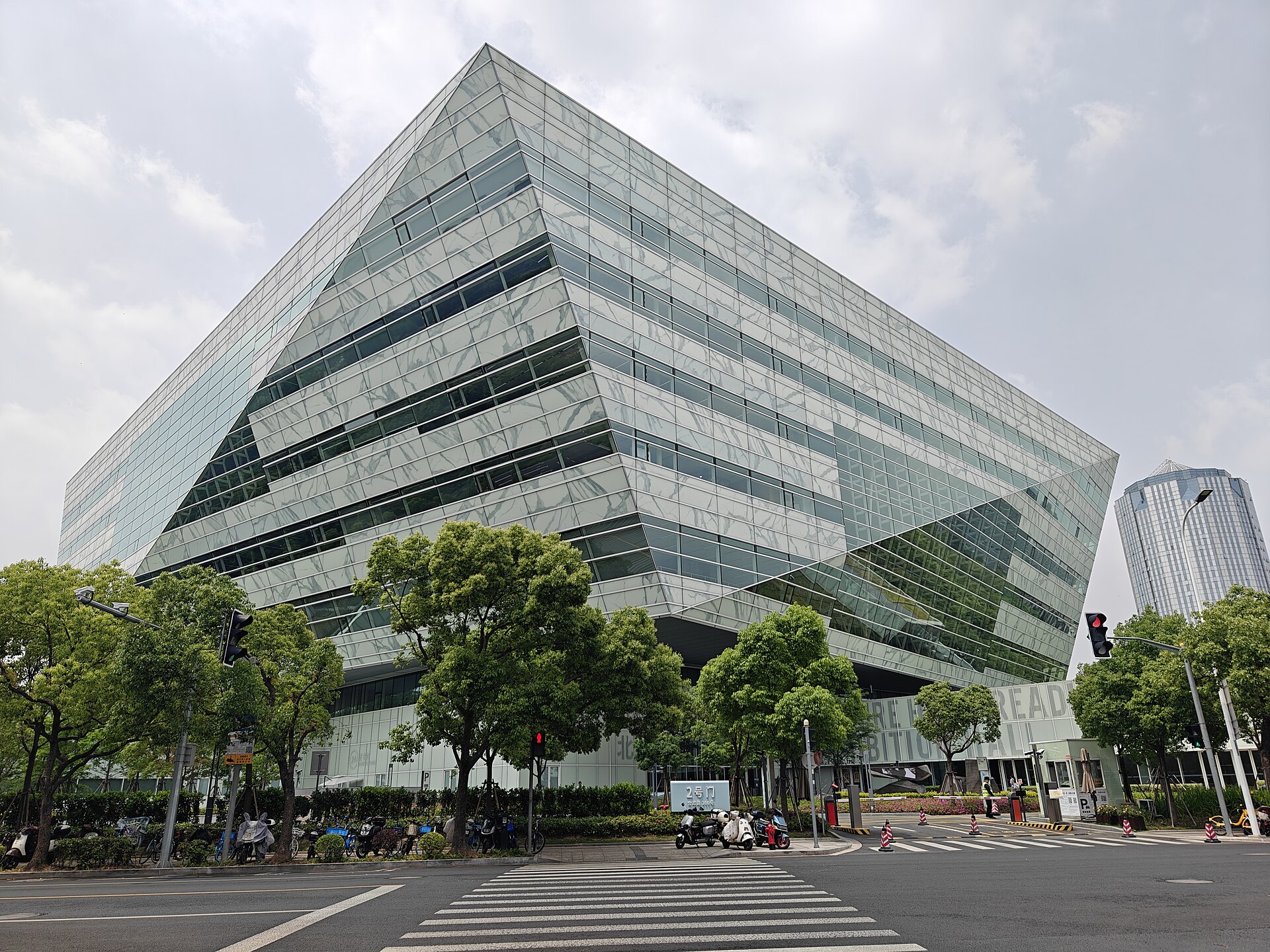 Faceted glass exterior of Shanghai Library East above a tree-lined street