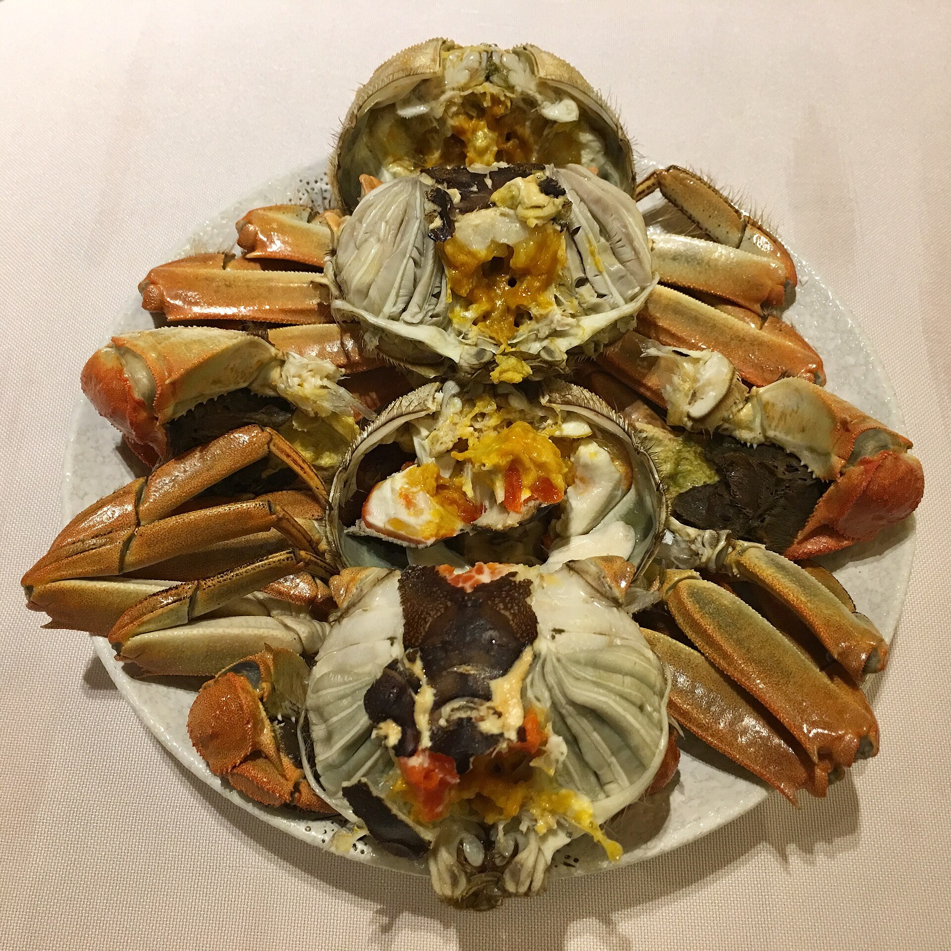 Several cooked mitten crabs opened to show shells, legs and roe on a plate
