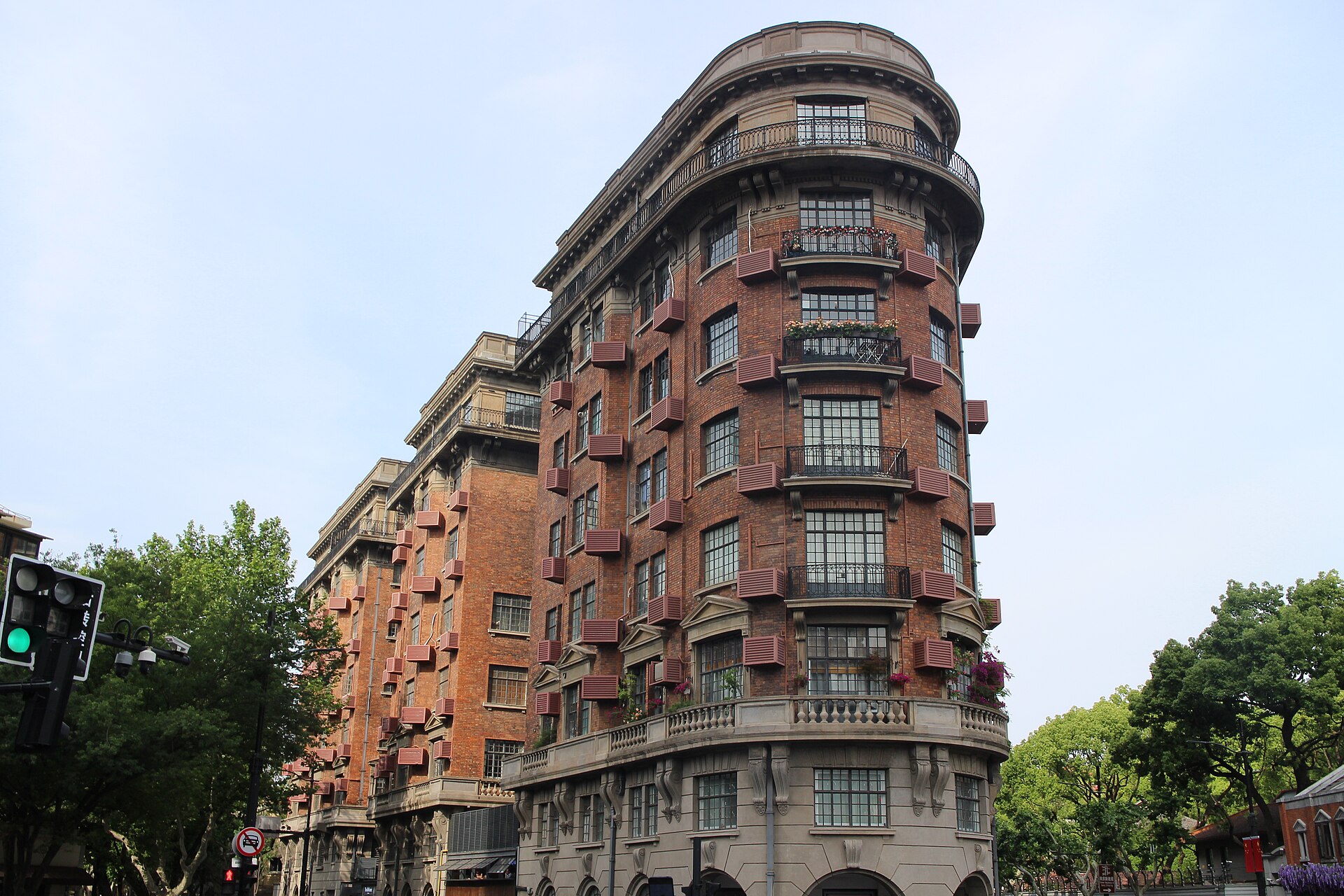 Red-brick Wukang Mansion curving to a narrow point at a tree-lined intersection