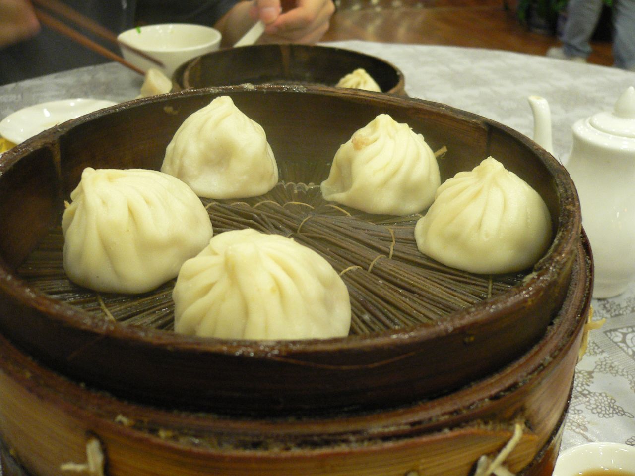 Six pleated xiaolongbao in a bamboo steamer on a restaurant table