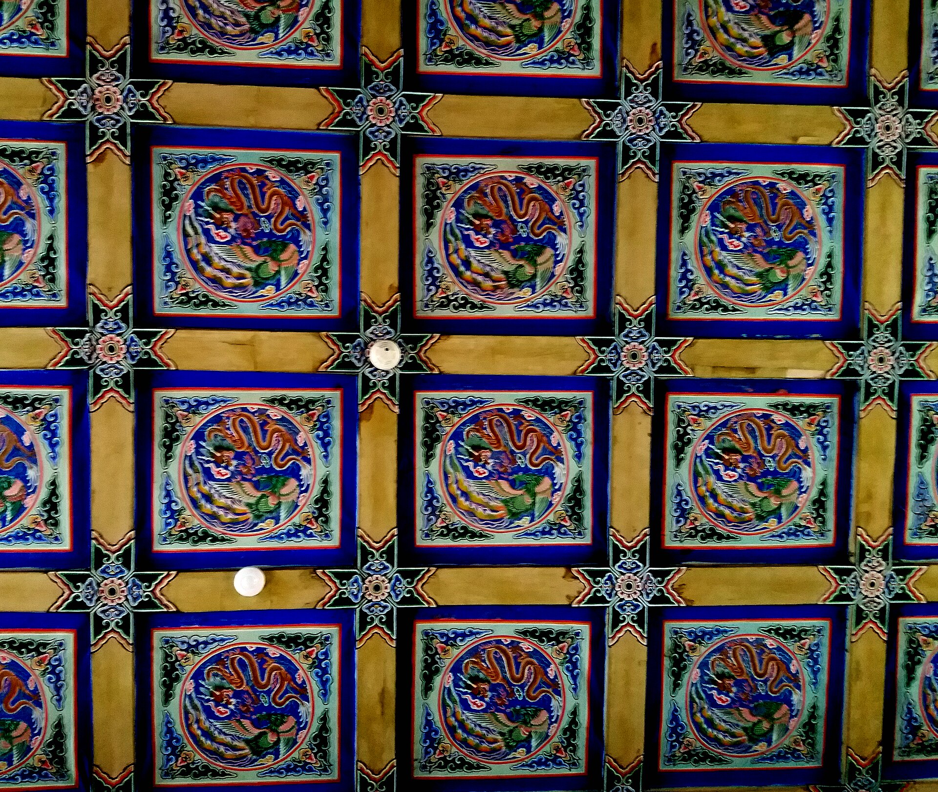 Repeated painted dragon medallions and modern lights on a palace ceiling