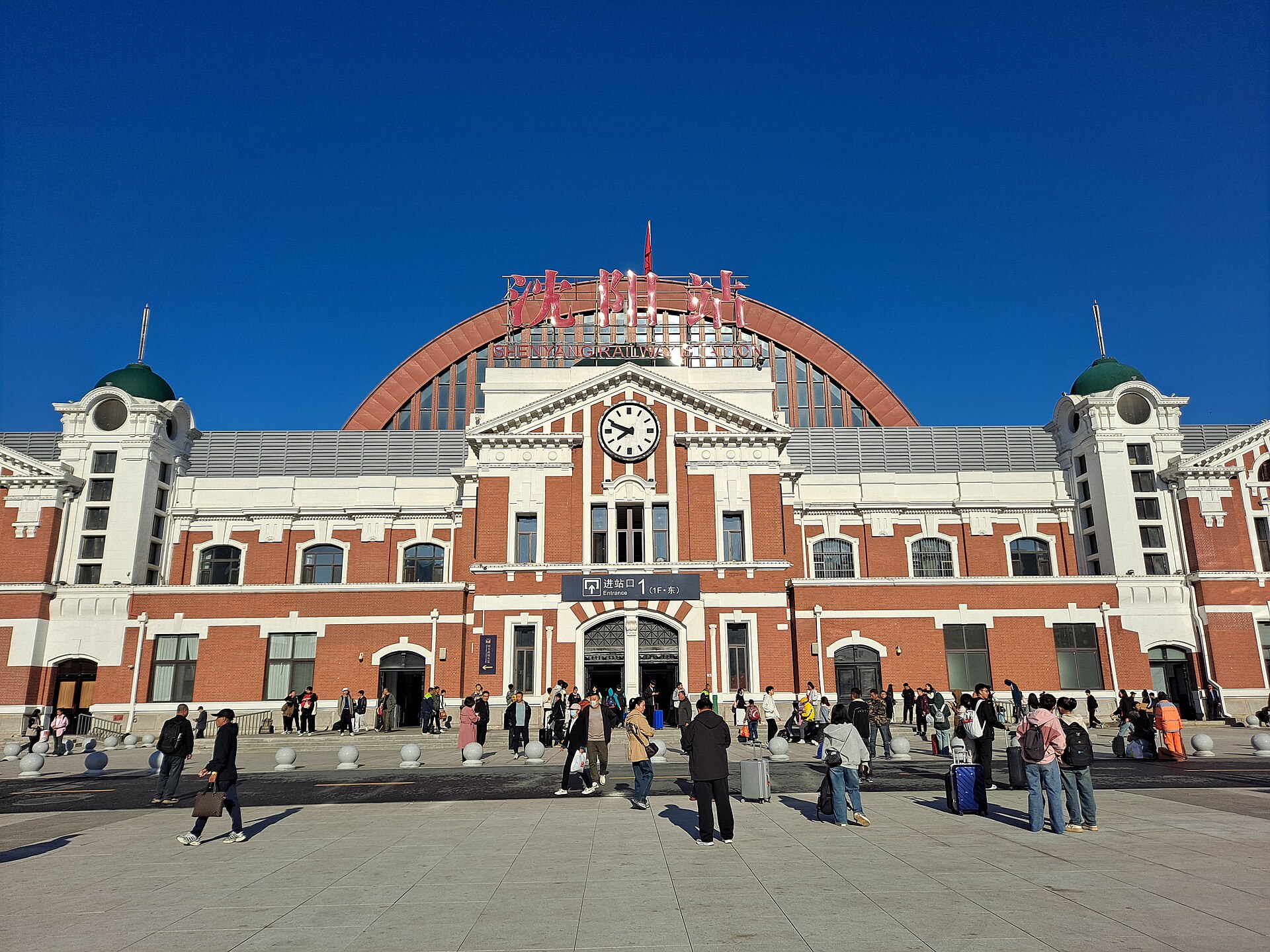 Red-and-white Shenyang Railway Station facade and passengers in 2024
