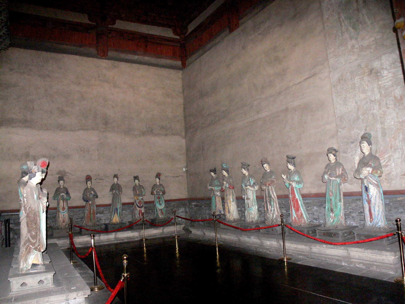 Painted maid sculptures behind a visitor barrier inside Jinci