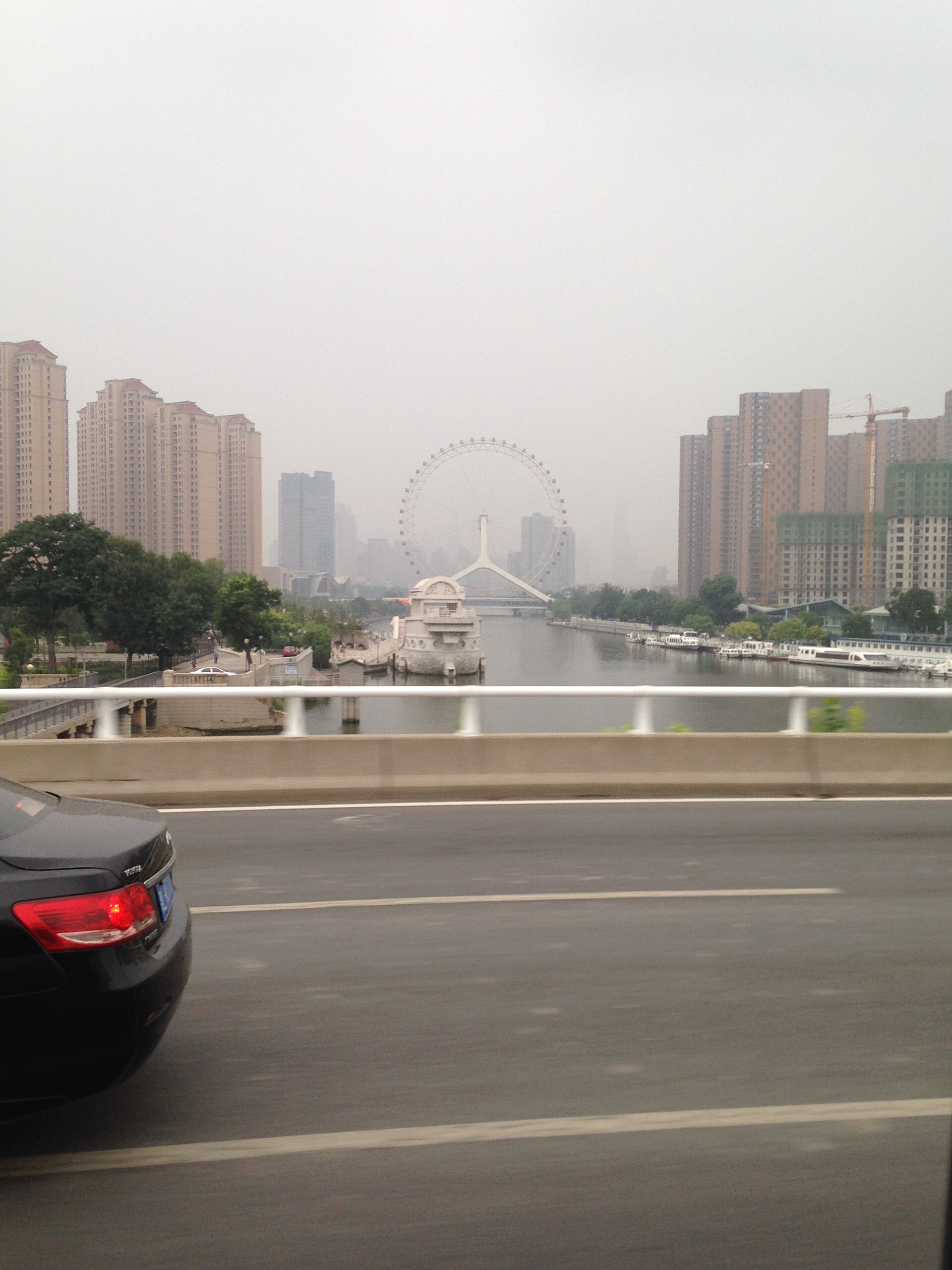 Tianjin Eye behind road barriers, traffic and high-rises in a dated view