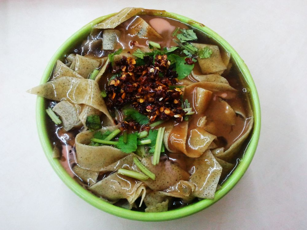 Top-down bowl of guobacai with cut crepe sheets, coriander and chili