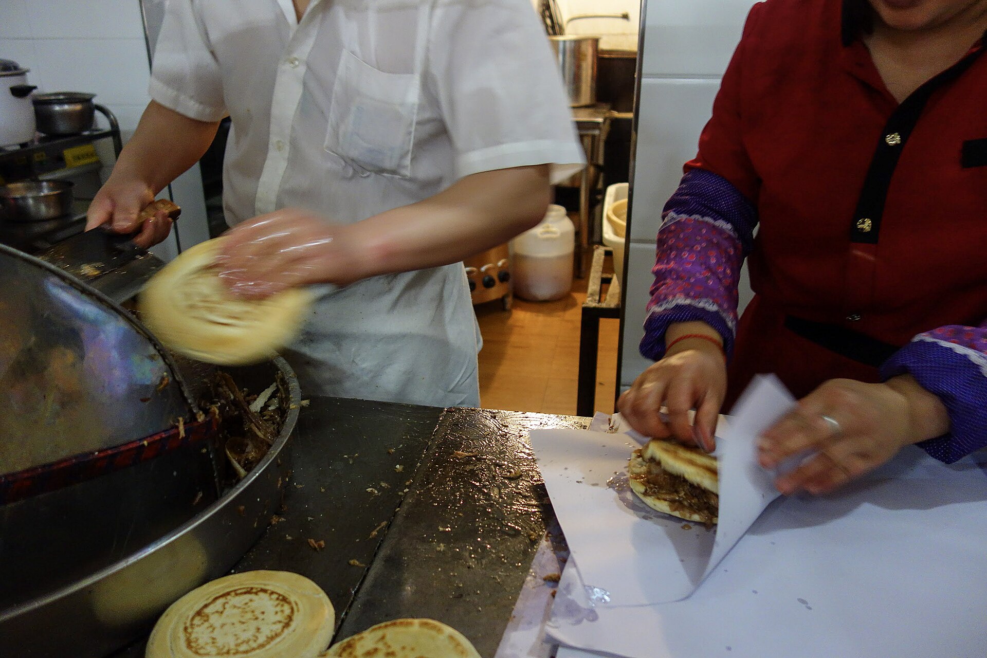 Two workers assembling roujiamo beside a heated pan