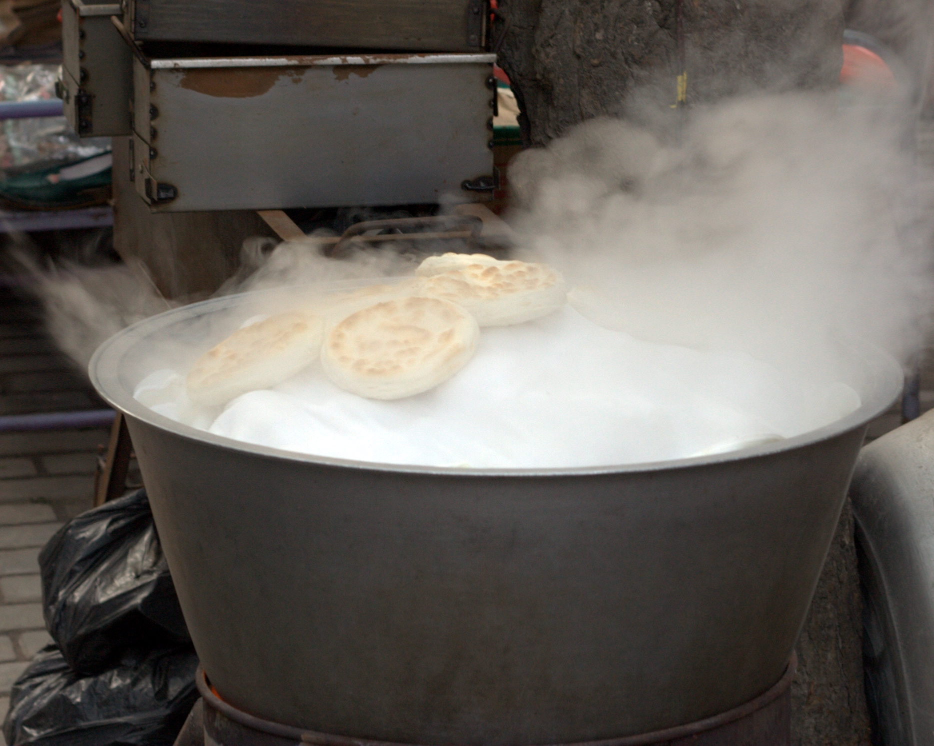 Round flatbreads surrounded by steam above a large metal vessel