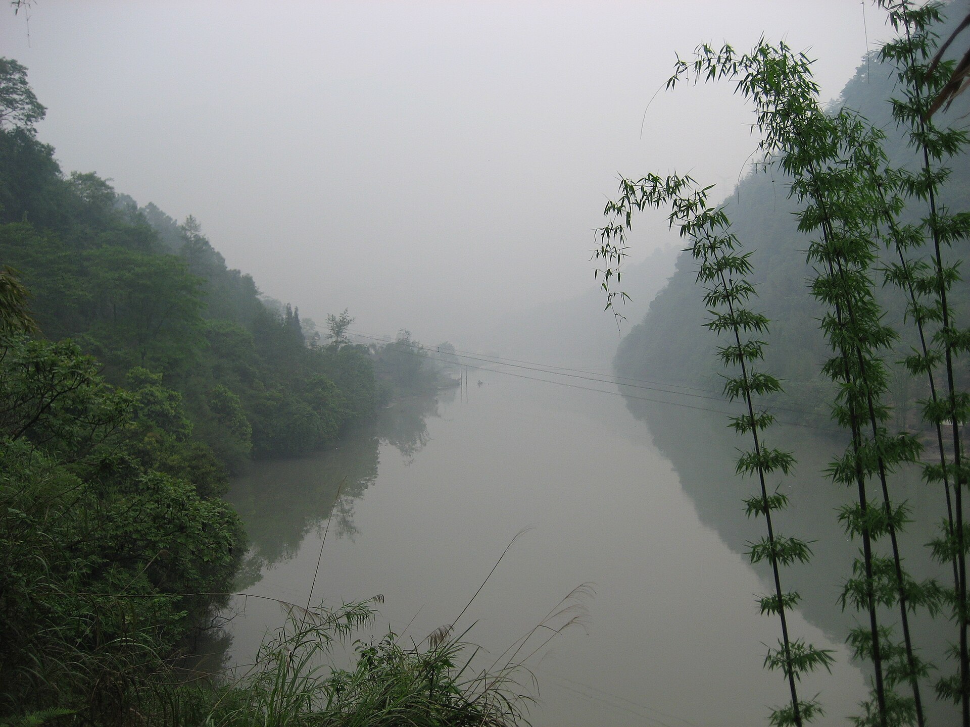 Misty wooded valley reflected in still water at Yingjing
